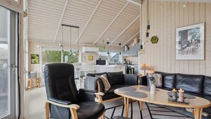 A modern interior with a wooden ceiling, a black leather sofa, a dining table, and a kitchen area. - Beautiful summer house from 2008 outdoor spa (Nakskov)