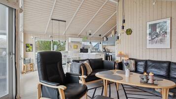 Et moderne interiør med træloft, en sort lædersofa, et spisebord og et køkkenområde.