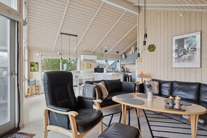 A modern interior with a wooden ceiling, a black leather sofa, a dining table, and a kitchen area. - Beautiful summer house from 2008 outdoor spa (Nakskov)