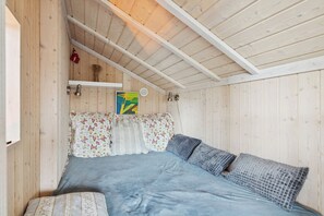A wooden-paneled room with a bed, pillows, a wall-mounted shelf, and a framed picture. - Beautiful summer house from 2008 outdoor spa (Nakskov)