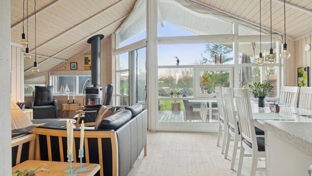 A spacious room with a large window, a fireplace, a sofa, and a dining area. - Beautiful summer house from 2008 outdoor spa (Nakskov)