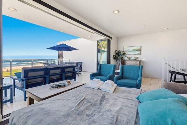 A modern living room with a view of the beach, a balcony with outdoor furniture, and a large window. - Ocean Park Combo 9 & 10 (San Diego)