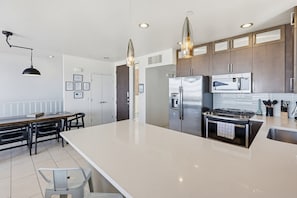 A modern kitchen with a large island, stainless steel appliances, and pendant lighting. - Ocean Park Combo 9 & 10 (San Diego)