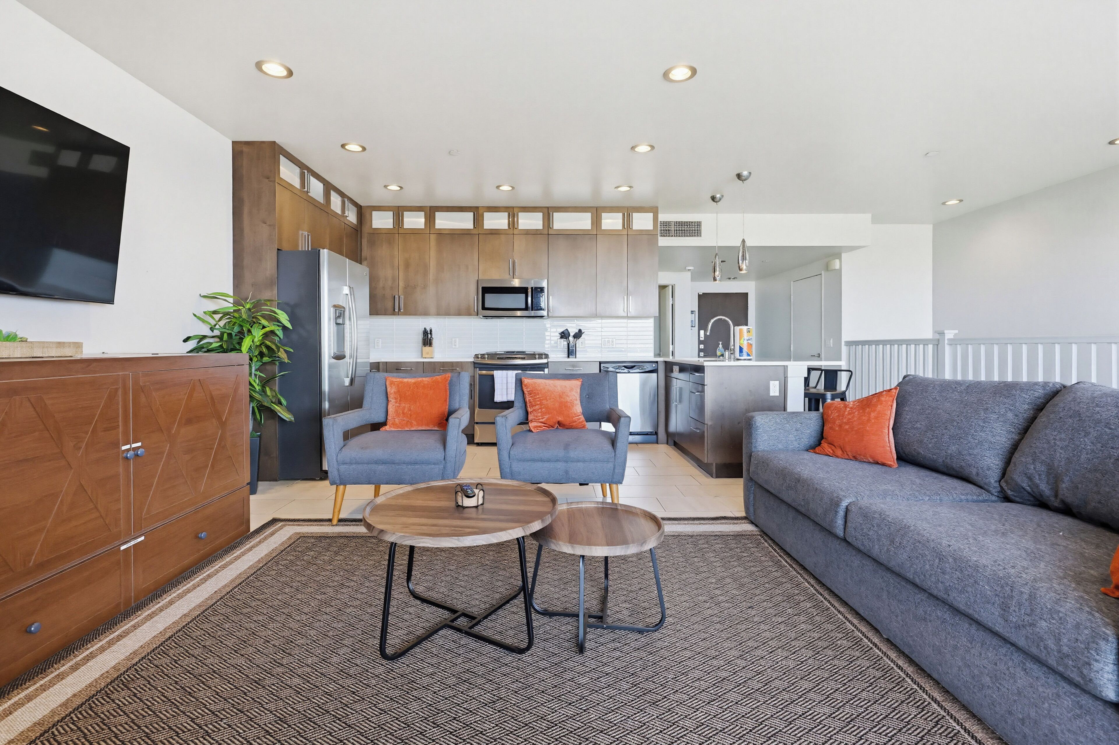 A modern kitchen with built-in appliances, a dining area with two chairs and a table, and a living room with a sofa and a coffee table.