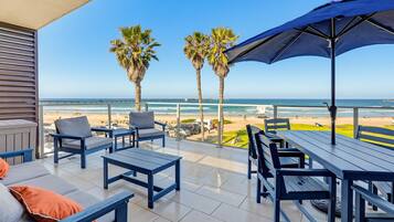 A terrace with outdoor seating, palm trees, and a view of the beach.