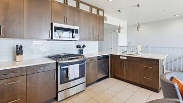A modern kitchen with stainless steel appliances, wooden cabinets, and a white countertop.