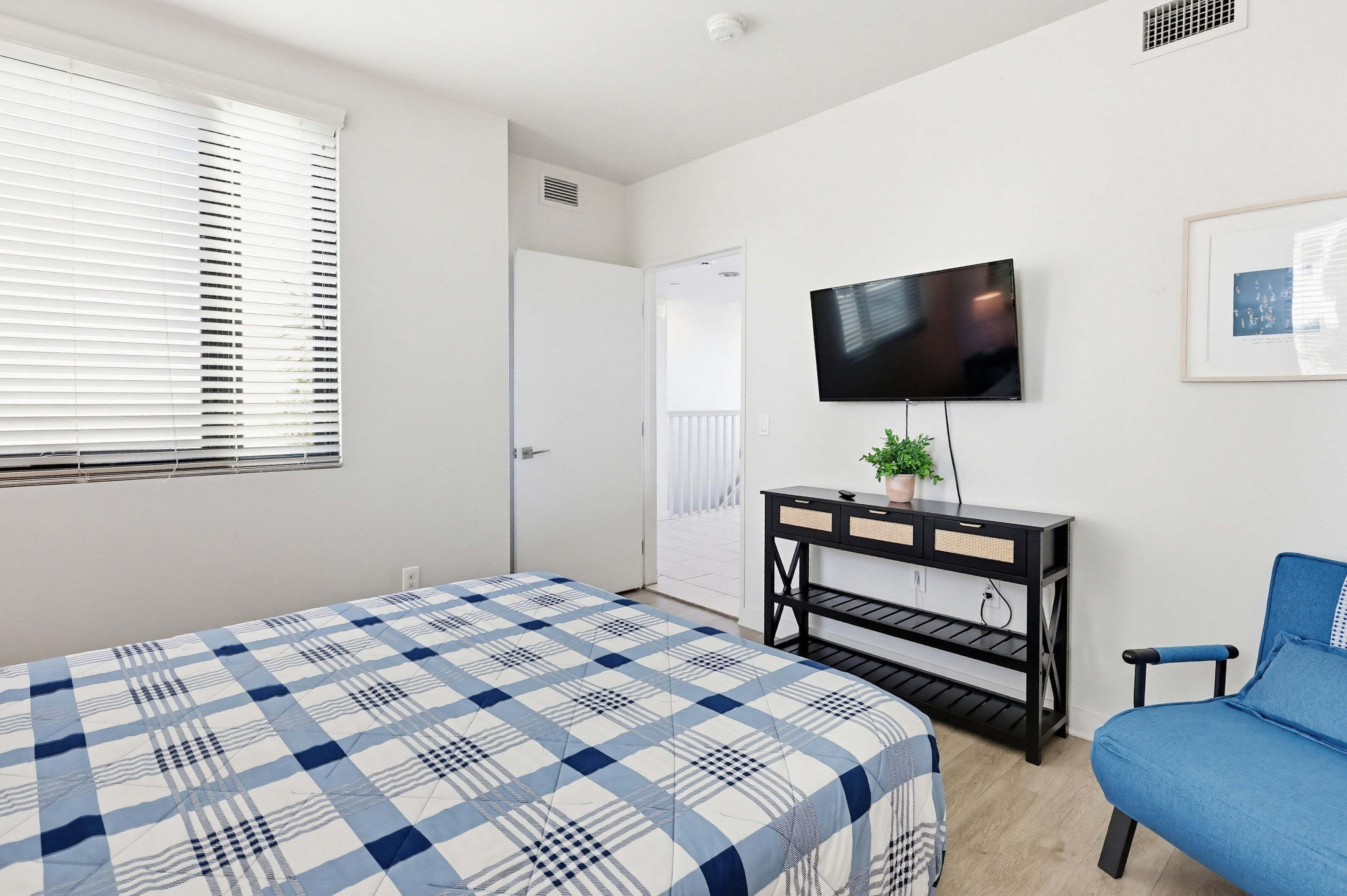 A bedroom with a bed, a TV, a desk, a chair, and a door leading to another room.