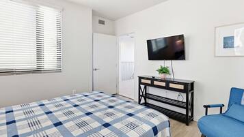 A bedroom with a bed, a TV, a desk, a chair, and a door leading to another room.