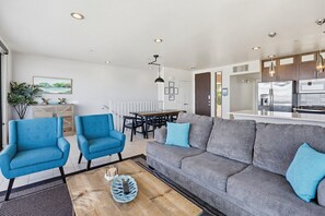 Ett modernt vardagsrum med en grå soffa, blå fåtöljer, ett träbord och en matplats med bord och stolar.