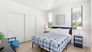 A bedroom with a bed, a desk, a chair, and a window with blinds. - Ocean Park Combo 9 & 10 (San Diego)