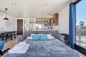Ein modernes Hotelzimmer mit einem großen Bett, einem Essbereich, einer Küchenzeile und Blick auf die Stadt.