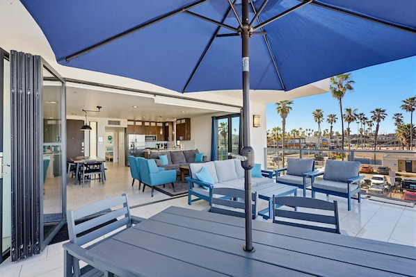 An outdoor patio with blue furniture, a large umbrella, and a view of palm trees and a cityscape. - Ocean Park Combo 9 & 10 (San Diego)