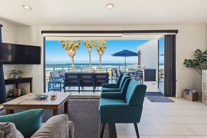 A modern living room with a large TV, a sofa, a coffee table, and a view of the ocean through a sliding door. - Ocean Park Combo 9 & 10 (San Diego)