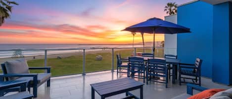 A balcony with a view of the ocean, outdoor furniture, and a blue umbrella.