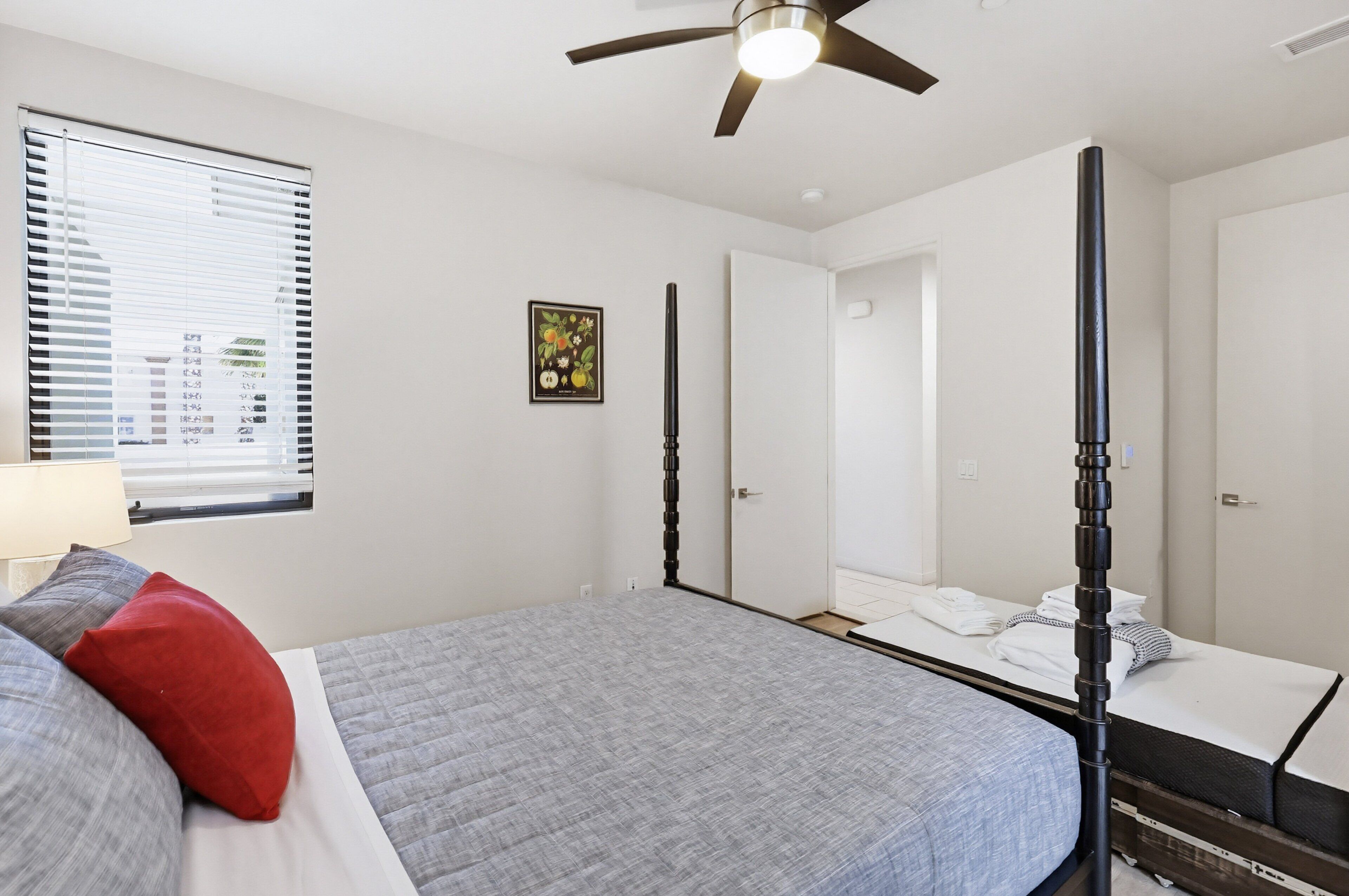 A bedroom with a bed, a ceiling fan, a window with blinds, and a door.
