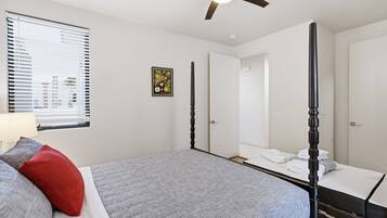 A bedroom with a bed, a ceiling fan, a window with blinds, and a door.