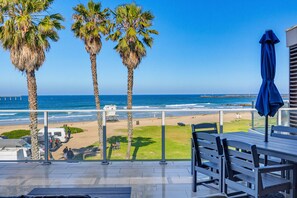 A balcony with a view of the beach, palm trees, and a lifeguard tower. - Ocean Park Combo 9 & 10 (San Diego)