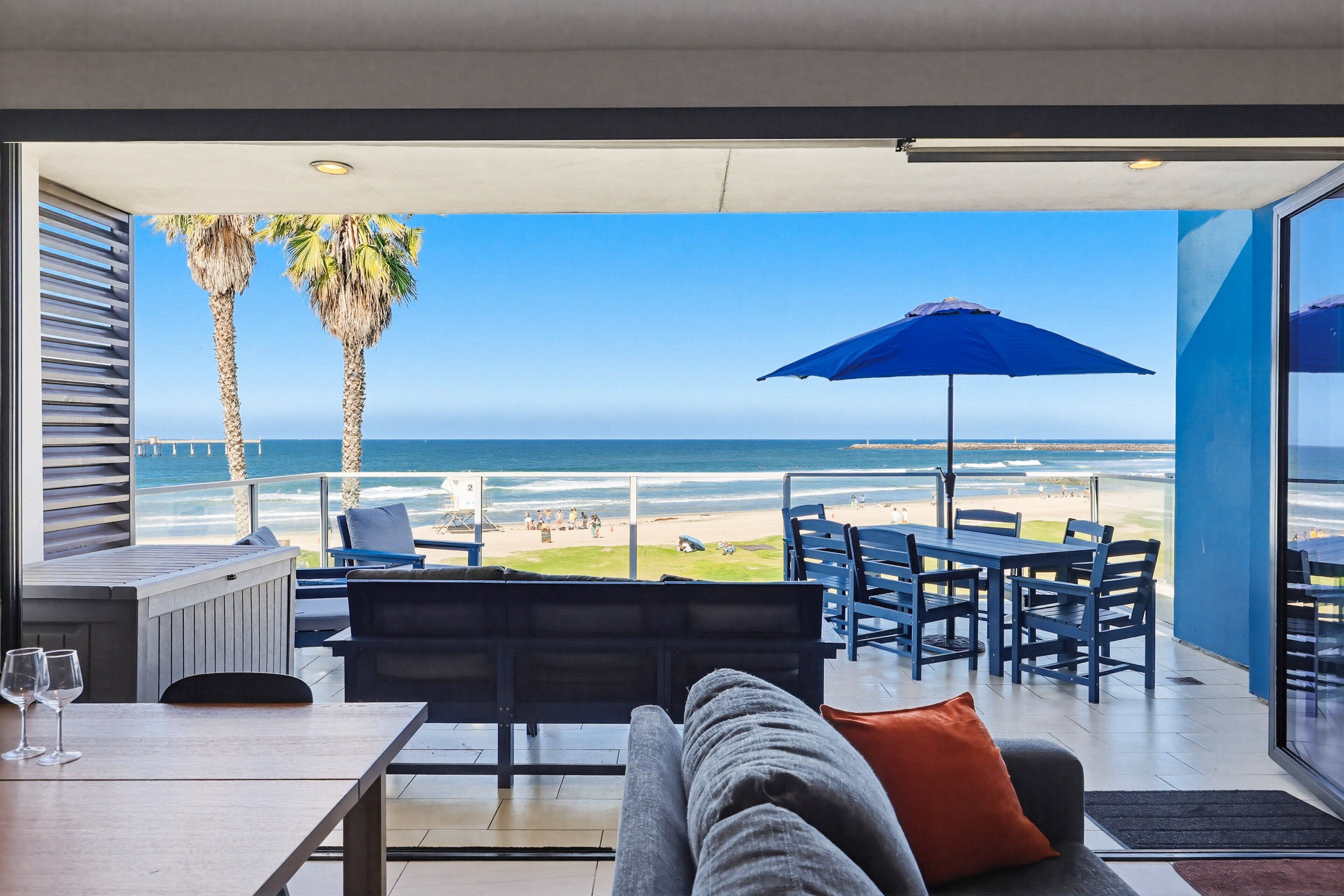 Una habitación moderna con vistas a la playa, un comedor y una zona de estar con un paraguas azul.