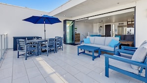 An outdoor patio with a dining table, chairs, a blue umbrella, and a sofa set. - Ocean Park Combo 9 & 10 (San Diego)