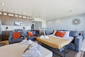 A modern hotel room with a bed, seating area, kitchenette, and a view of the city. - Ocean Park Combo 9 & 10 (San Diego)