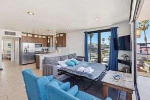 A modern hotel room with a kitchenette, a sofa bed, a dining table, and a large window with a view of palm trees. - Ocean Park Combo 9 & 10 (San Diego)