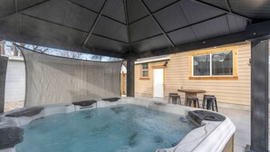 Ein Whirlpool mit überdachter Terrasse, einem Holzzaun und einem Haus mit Fenster und Tür.