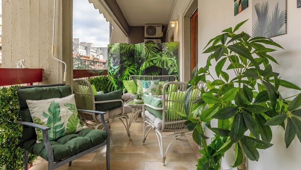 Un balcon avec des fauteuils à coussins verts, une table et des plantes en pot.
