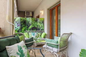 Un balcone con mobili in vimini, cuscini verdi e uno sfondo a tema tropicale.