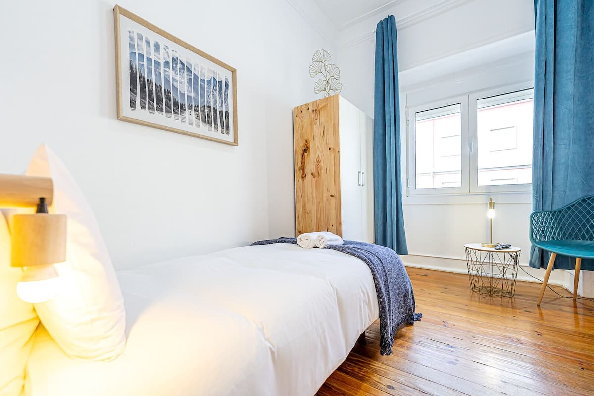 Una camera da letto con un letto, un armadio in legno, una sedia, un tavolino e una finestra con tende.