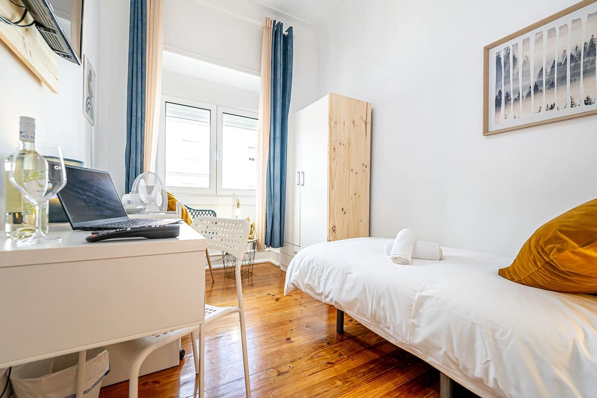 Una camera da letto con un letto, una scrivania con un portatile, una sedia e una finestra con tende.