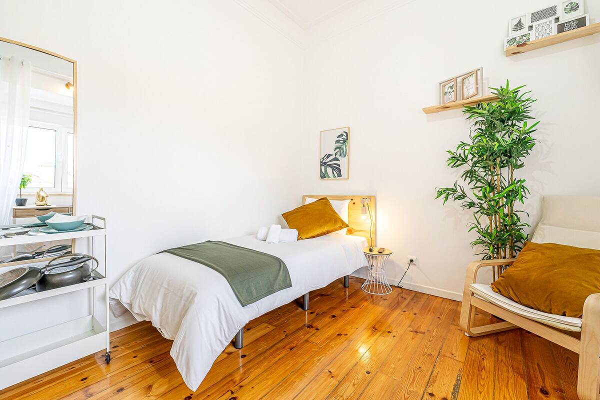 Una camera da letto con un letto, comodino, lampada, sedia e una pianta.