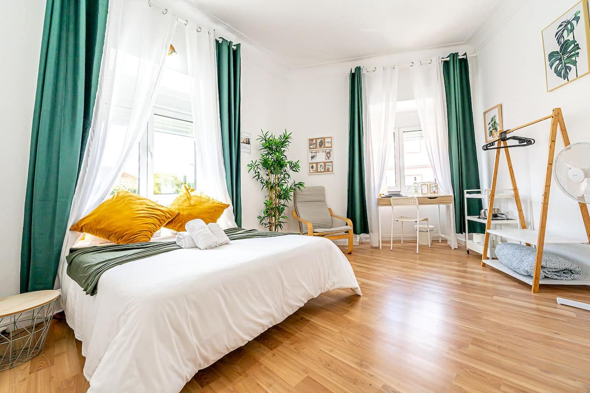 Una camera da letto con un letto, una scrivania, una sedia, una pianta e una ventola.