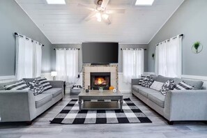 Ein Wohnzimmer mit zwei grauen Sofas, einem schwarz-weißen Schachbrettteppich, einem Kamin und einem Deckenventilator.