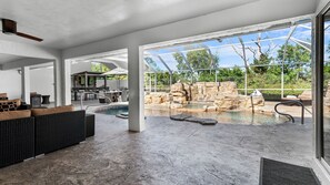 Ein moderner Poolbereich im Freien mit einem Wasserfall aus Stein, Liegebereich und einer überdachten Terrasse.