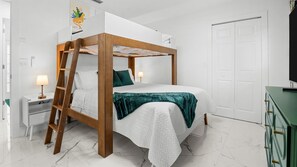 Ein Bett mit Baldachin, dessen Gestell aus Holz gefertigt ist, mit weißer Bettwäsche, einer grünen Decke, einem Nachttisch mit Lampe und einem grünen Kommodenstück.