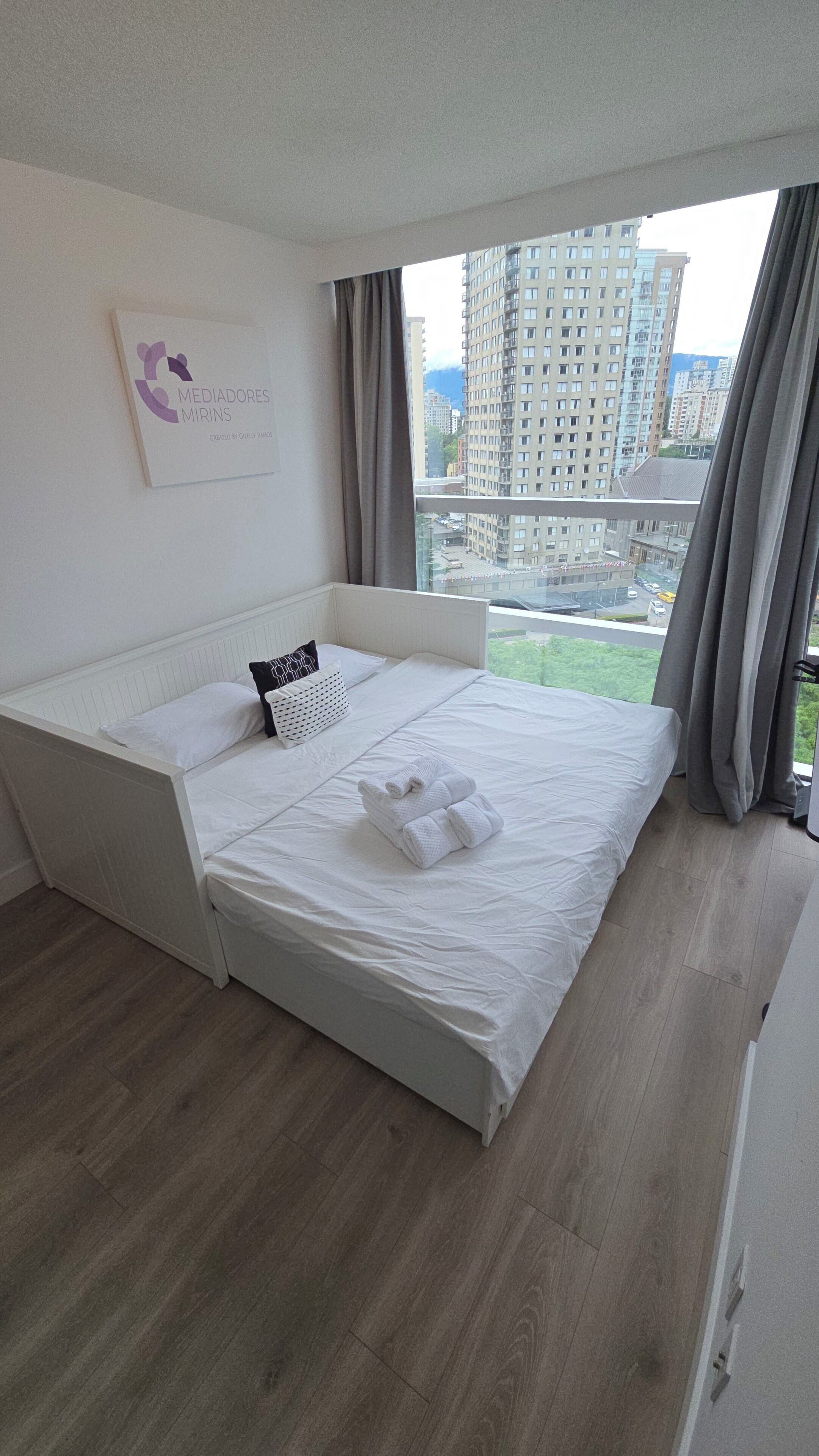 A modern bedroom with a bed, a wall-mounted artwork, and a city view.