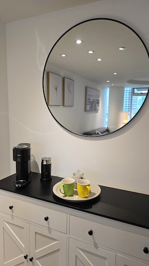 Ein runder Spiegel an der Wand, eine Kaffeemaschine, zwei Tassen und ein Tablett.