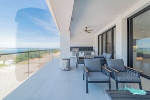 A balcony with a modern kitchen, grey seating, and a view of the sea.