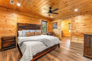 Ein Schlafzimmer einer Holzhütte mit einem großen Bett, einem Deckenventilator und einem Holz-Kopfteil.