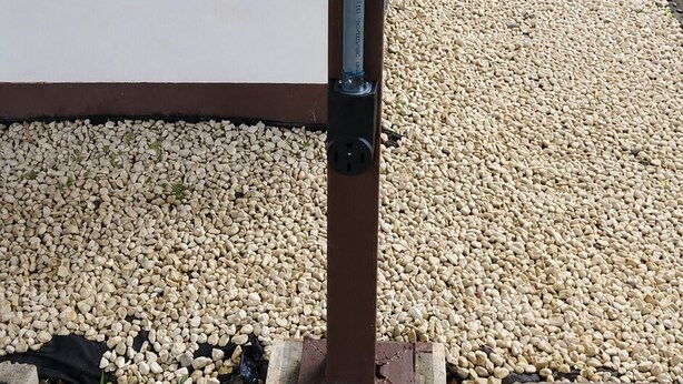 Schild für eine Ladesäule für Elektrofahrzeuge an einem Pfahl, im Hintergrund ein Kiesweg und Pflanzen.