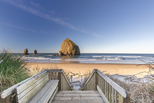 A wooden staircase leading to a beach with a large rock formation in the distance.
