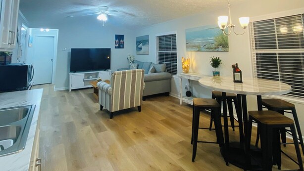 A modern kitchen with a built-in oven, a dining area with a round table and bar stools, a sofa, and a TV in the living area. - Cozy home in the heart of Calabash NC (Calabash)