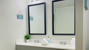 A bathroom with two mirrors, a sink, a potted plant, and a towel rack. - Cozy home in the heart of Calabash NC (Calabash)