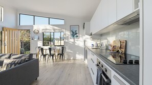 A modern kitchen with white cabinets, a stainless steel countertop, and a dining area with a grey sofa and chairs.