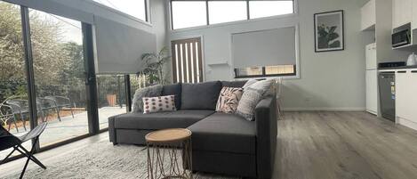 Ein modernes Wohnzimmer mit einem grauen Sofa, einem runden Beistelltisch und Blick ins Freie durch große Fenster.