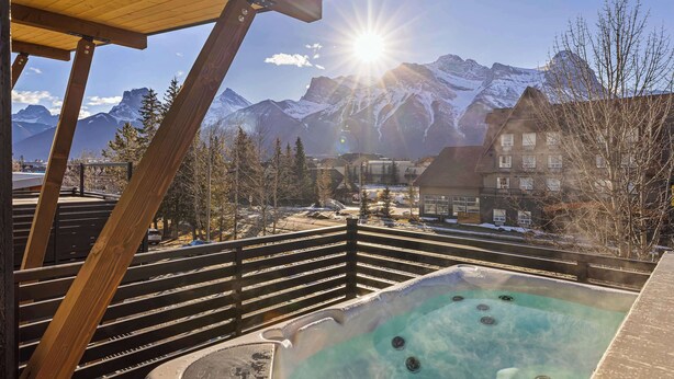 Un bain à remous avec vue sur les montagnes, une terrasse en bois et un ciel dégagé.
