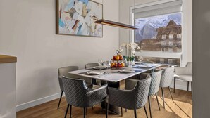 Un coin repas avec une table dressée pour quatre personnes, un tableau accroché au mur et une vue sur les montagnes par la fenêtre.
