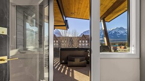Un intérieur moderne avec une porte vitrée donnant sur un balcon doté d’un plafond en bois, d’un coin salon et d’une vue sur des montagnes enneigées.