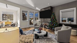 Un salon moderne avec une cheminée, un grand téléviseur à écran plat, un sapin de Noël et un coin salon confortable.