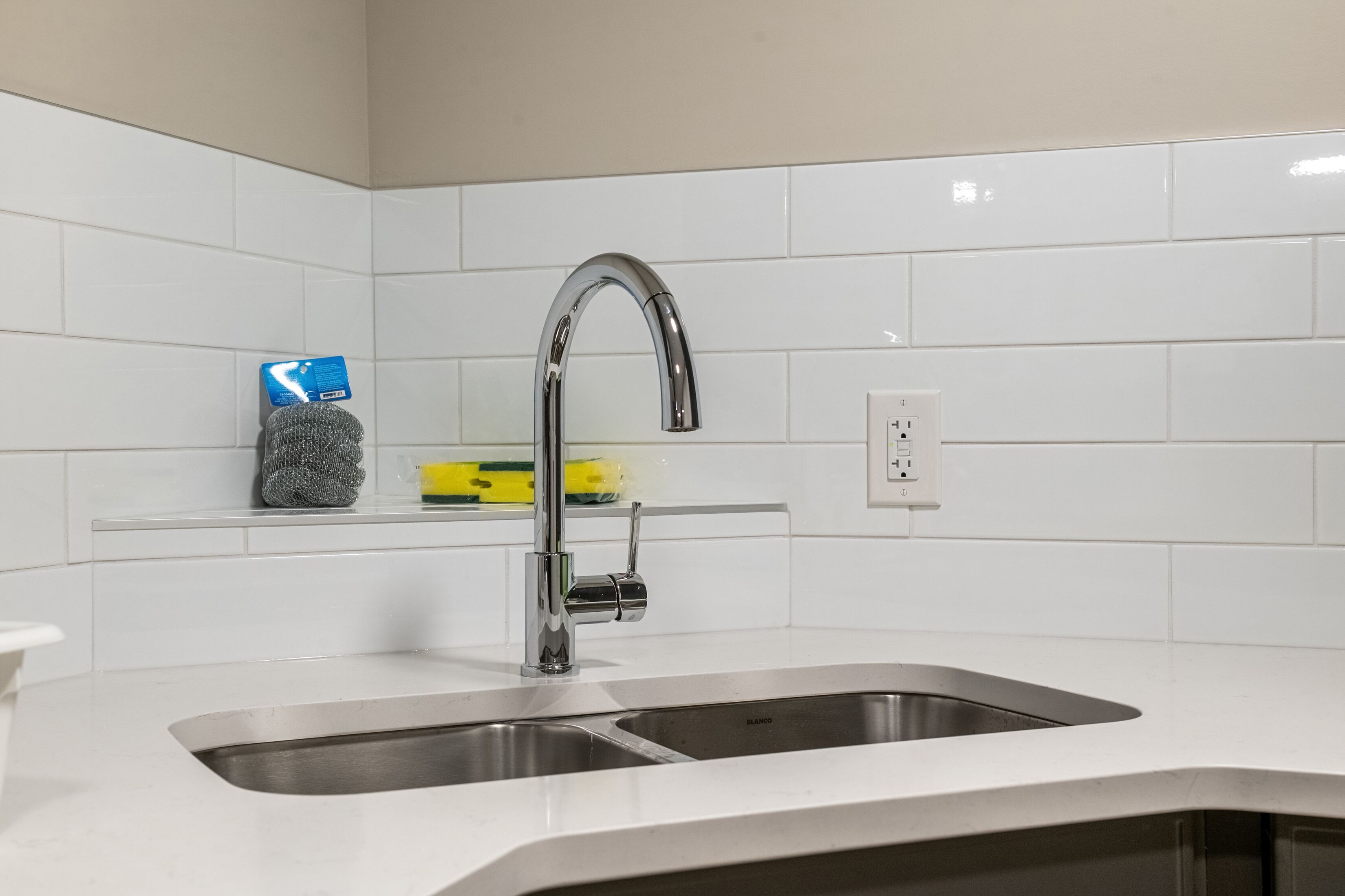 A modern kitchen with a stainless steel sink, a faucet, and a shelf with cleaning supplies.